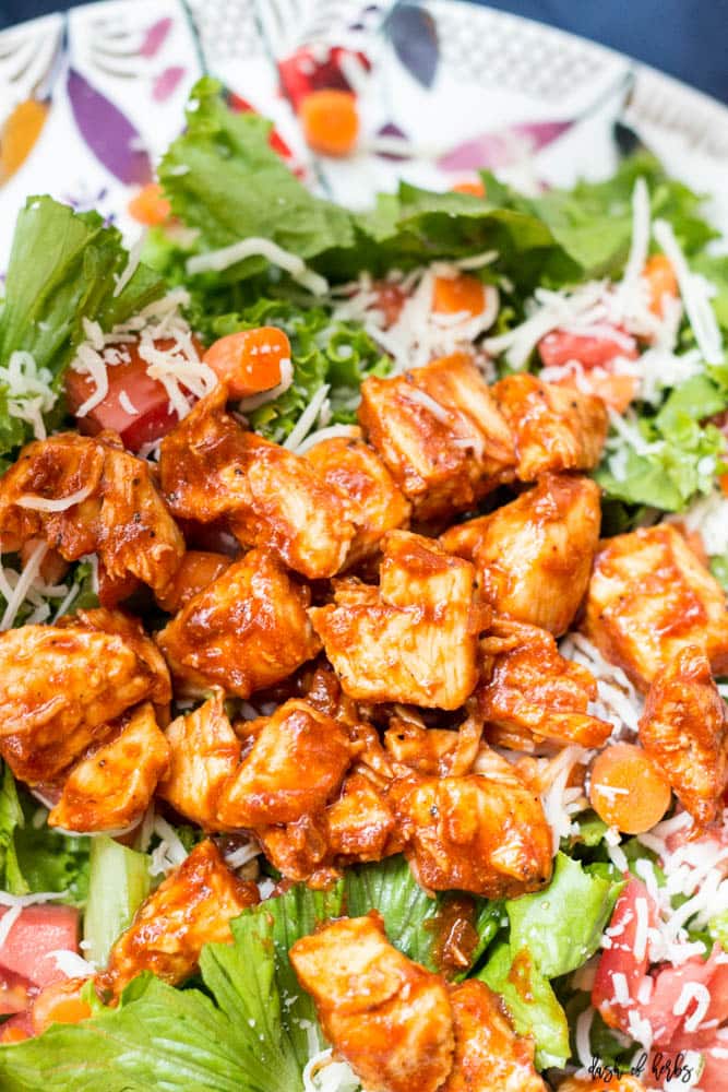 This image is a close up of the BBQ Chicken Salad recipe. The salad is on a colorful plate that has the BBQ chicken, chopped tomatoes, chopped romaine lettuce and sliced carrots in the image.