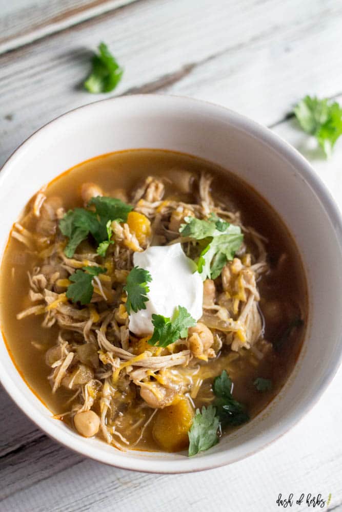 A close up image of the Slow Cooker White Chicken Chili recipe in a white bowl.  The shredded chicken, butternut squash and chickpeas.  The chili is topped with a dollop of Greek Yogurt.
