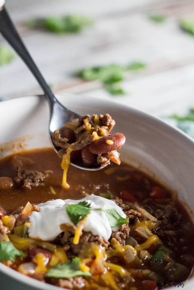 A close up image of the One Pot Easy Beef Chili recipe in a white bowl.  You can see the cooked beef, beans, shredded cheese and a dollop of Greek yogurt in the image.