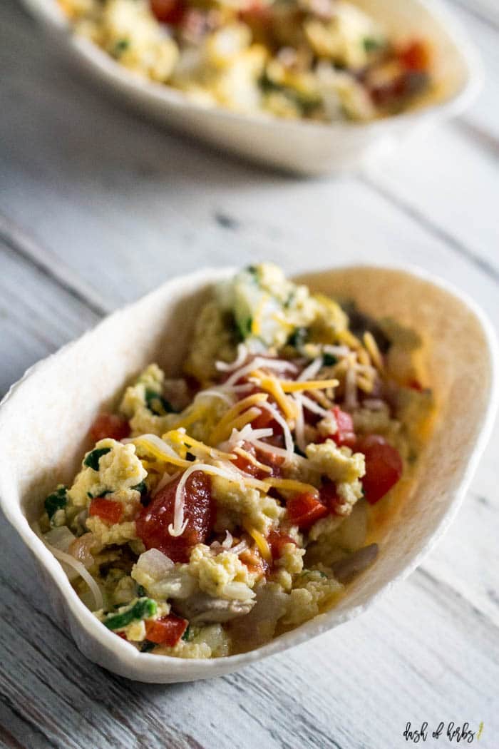 A close up image of the Southwest Breakfast Bowls recipe that shows a tortilla bowl vertically.  You can see the eggs, spinach, mushrooms and tomatoes covered with cheese.