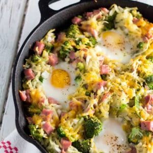 An image of the breakfast hash brown skillet recipe that shows off the cast iron skillet. It's a close up image that shows the ham, broccoli, eggs, cheese and hash browns.