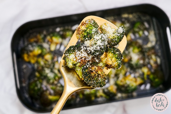 A close up shot of the air fryer garlic parmean broccoli on a golden spatula.  The pan of broccoli is below.