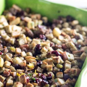 A close up image of the Apple Sausage Cranberry Stuffing recipe in a green colorful ceramic pan. You can see the dried cranberries, apples, stuffing and sausage in the image.