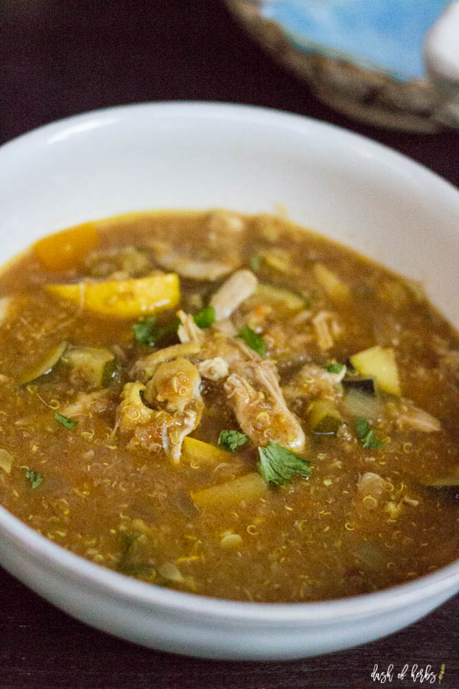 A close up image of the Slow Cooker Moroccan Chicken Soup recipe.  The soup is in a white bowl and it's filled with shredded chicken, zucchini, squash, quinoa